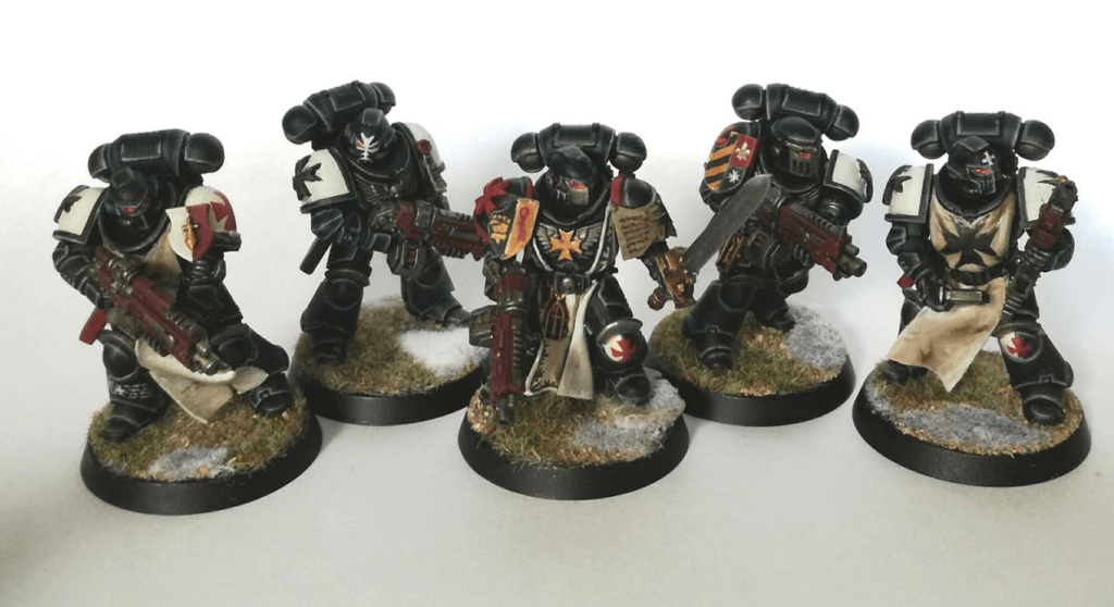 Five Black Templar models, painting in dark armor with white and red accenting on shoulder pads and guns. The middle model has a sword as well as a gun.