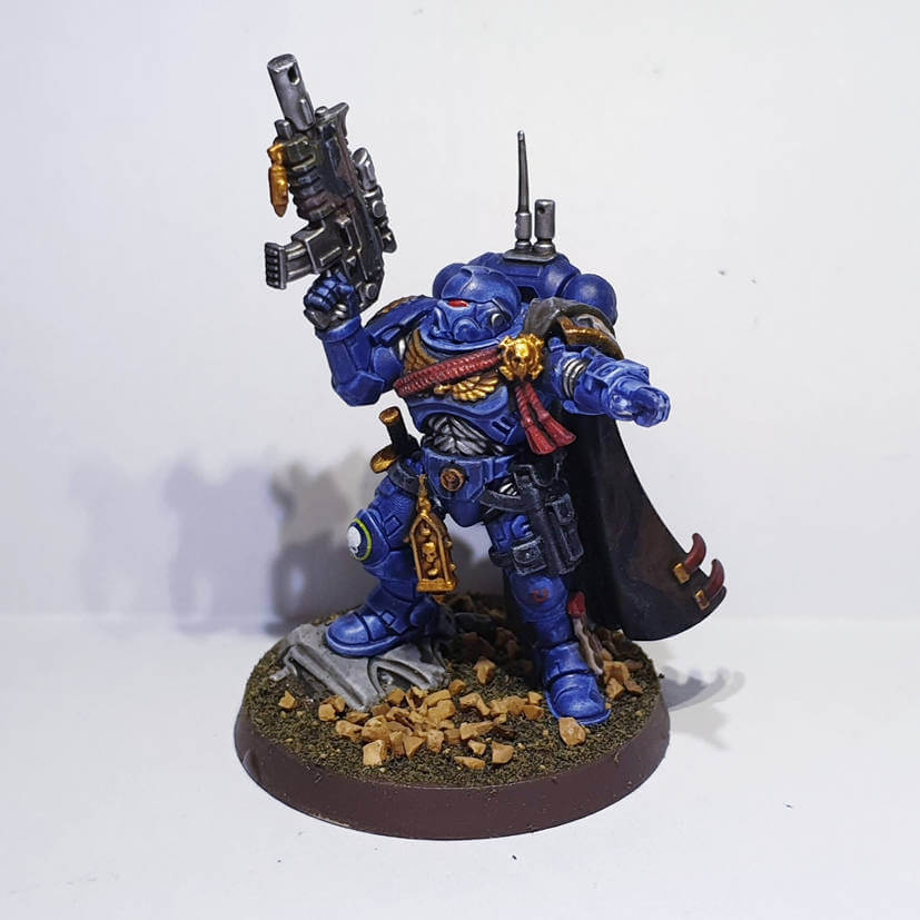 Painted Primaris Captain miniature in blue and gold armor, holding a bolt pistol and commanding forward.